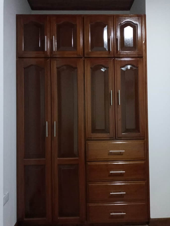 Clóset de madera estilo clásico barnizado en tono nogal, con seis puertas molduradas y cinco cajones centrales, con manijas metálicas verticales.