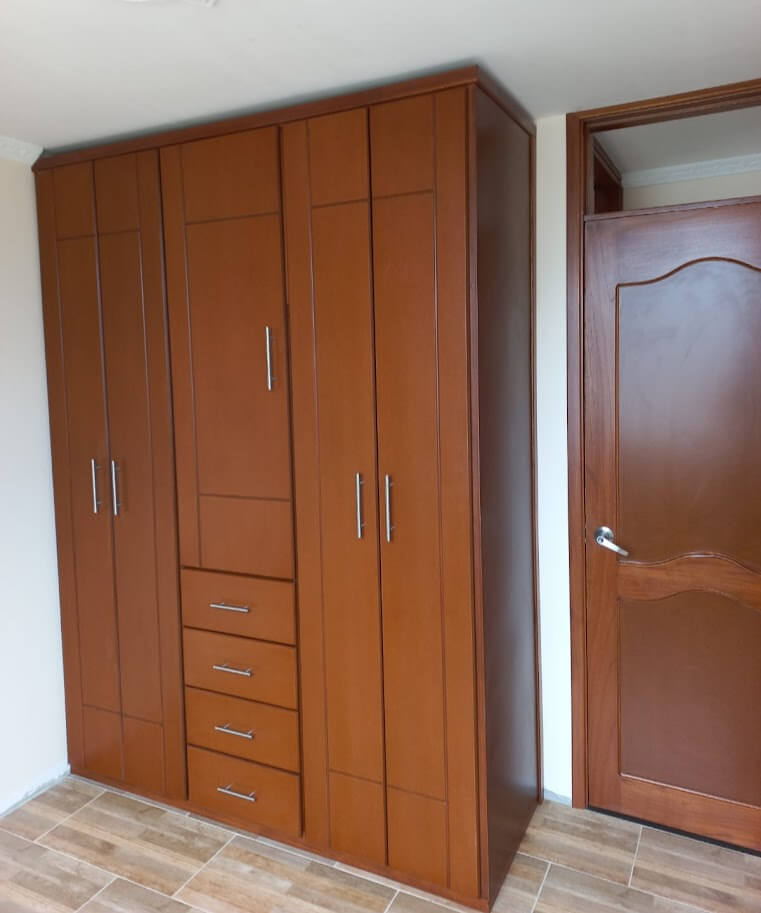 Clóset de madera color miel con diseño contemporáneo de líneas rectas, cinco cajones centrales y múltiples puertas abatibles, con manijas metálicas verticales.