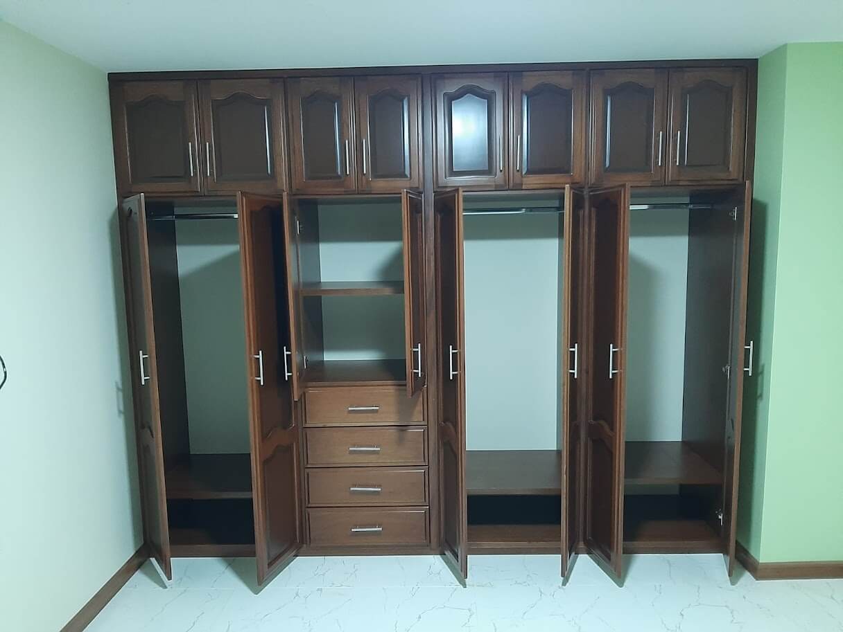 Clóset de madera estilo clásico en color nogal, con puertas molduradas, cajones centrales y compartimientos superiores, equipado con manijas metálicas rectos.