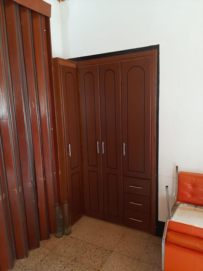 Clóset esquinero de madera estilo clásico en color caoba rojizo, con puertas altas molduradas, tres cajones inferiores y manijas metálicos plateados.