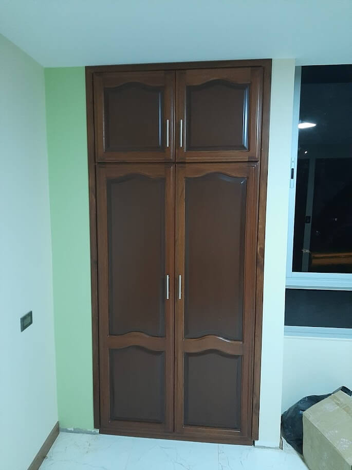 Clóset de madera estilo clásico en color nogal oscuro, con cuatro puertas molduradas y compartimientos superiores, manijas metálicas verticales.