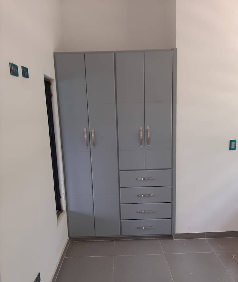 Clóset empotrado de estilo contemporáneo en color gris claro, con diseño liso de líneas rectas, cinco cajones centrales, seis puertas abatibles y manijas metálicas curvas.