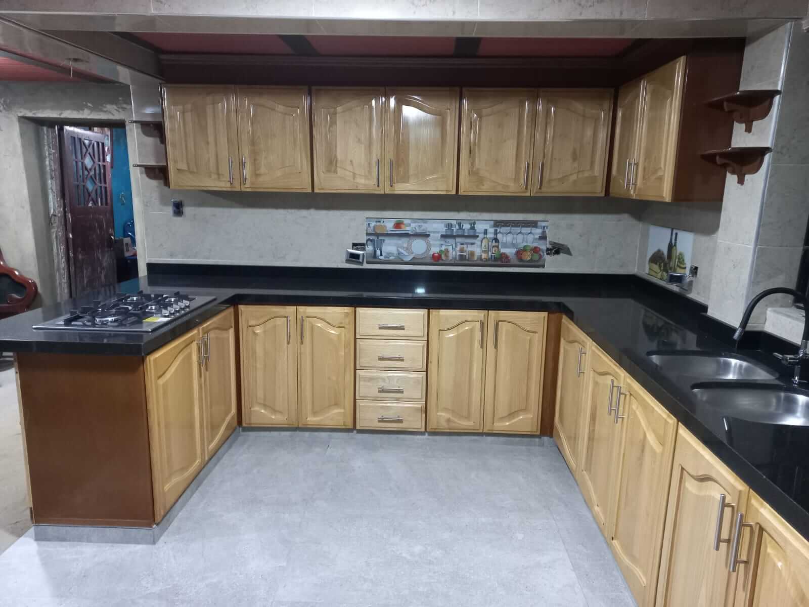 Cocina en forma de U con gabinetes de madera tono miel, mesón de granito negro, estufa empotrada de cuatro puestos y doble lavaplatos de acero inoxidable.