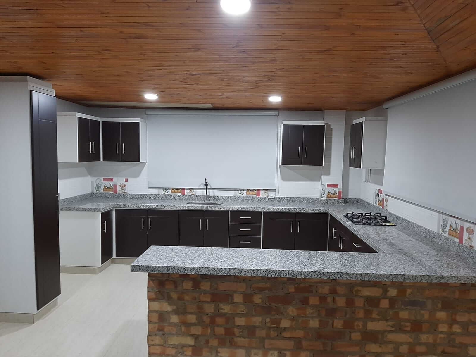 Cocina moderna con gabinetes de madera tono wengué, mesón de granito gris y estufa empotrada